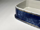 a blue and white ceramic dish with a gold rim