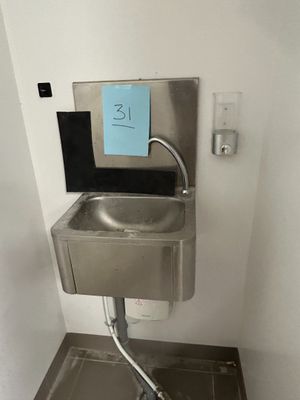 un lavabo en inox dans une salle de bains, avec une pancarte bleue accrochée au mur