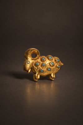 une photo représentant une figurine de bélier en or et en turquoise posée sur une table