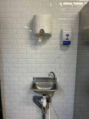 un lavabo dans des toilettes publiques, avec un distributeur de serviettes en papier fixé au mur