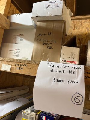 une pile de cartons posée sur une étagère, sur laquelle est accrochée une pancarte