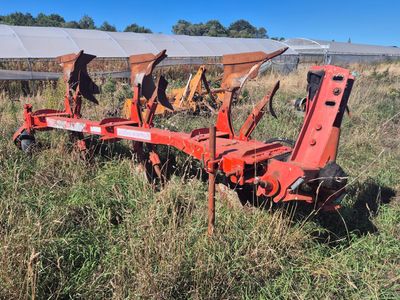 une charrue rouge attachée à un tracteur, au milieu d'un champ