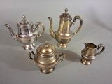 trois théières en argent et une cafetière sur une table