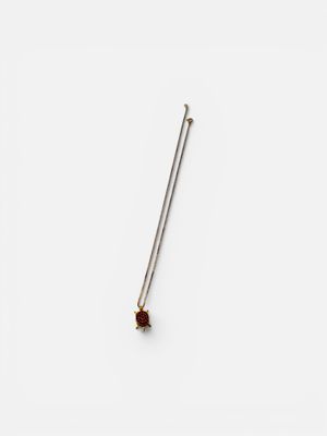 a close up of a metal pin with a red stone on it