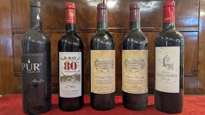 six bottles of wine are lined up on a red table cloth