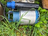 a water pump sitting in the grass next to a pipe