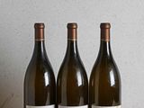 three bottles of wine sitting on a wooden table next to a bottle of wine