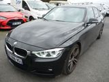 une BMW Série 3 noire garée sur un parking, avec d'autres voitures en arrière-plan