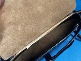 someone is holding a brown purse with a black handle on a blue surface