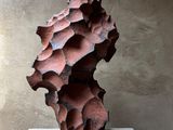 une sculpture abstraite représentant un arbre, posée sur un socle devant un mur