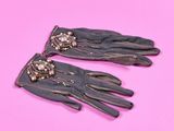 une paire de gants en cuir noir ornés de perles sur fond rose