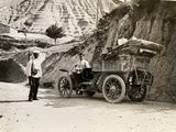 a black and white photo of a man standing next to an old car