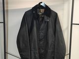 une veste en cuir noir accrochée à un portant devant un mur blanc