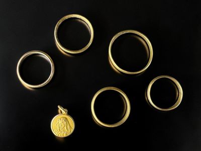 plusieurs bagues en or et une pièce d'or posées sur une surface noire
