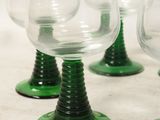 four green wine glasses sitting on top of a white table