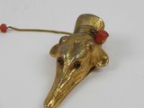 brass figurine of a bird wearing a hat and a red bead