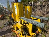 un homme debout sur une machine jaune, à côté d'un tas d'arbres