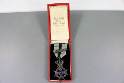 une image représentant une médaille d'argent ornée d'un ruban violet, dans un coffret rouge