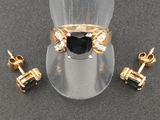 une paire de boucles d'oreilles en diamant noir et blanc et une bague en or, présentées sur un porte-bagues transparent