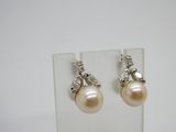 une paire de boucles d'oreilles en perles et diamants exposée sur un fond blanc