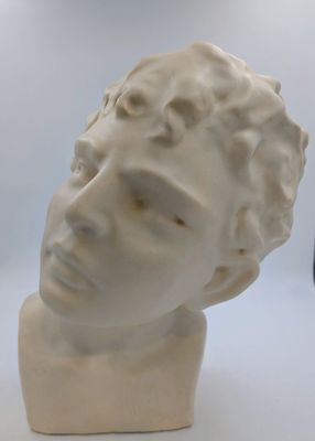 une sculpture blanche représentant un homme aux cheveux bouclés, posée sur une surface blanche