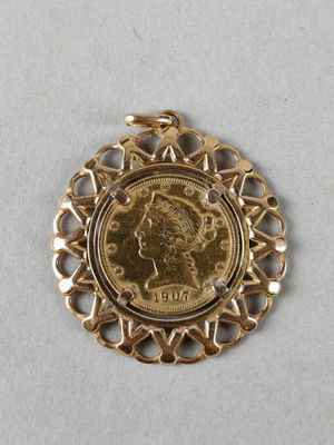un gros plan d'une pièce de monnaie sertie dans un pendentif en or, posée sur une surface blanche