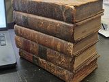 des livres empilés les uns sur les autres sur un bureau, avec un ordinateur portable en arrière-plan