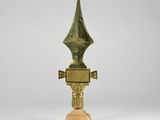 une image représentant un trophée en or au sommet pointu, posé sur un socle en bois