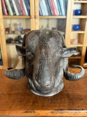 statue représentant une tête de bélier posée sur une table en bois devant une bibliothèque