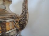 a silver tea pot sitting on a table next to a white wall