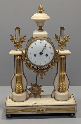 une horloge blanche et dorée posée sur un socle, elle-même posé sur une table