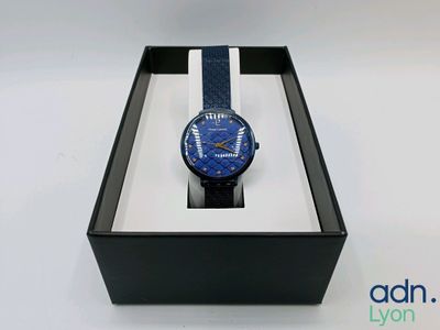 une image représentant une montre dans un coffret noir orné d'une bande bleue et blanche