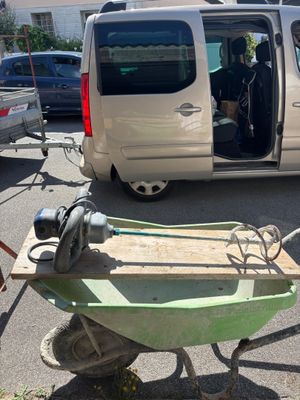 une brouette verte sur le parking, à côté d'une camionnette blanche