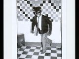black and white photograph of a man in a suit and tie standing in front of a checkered wall