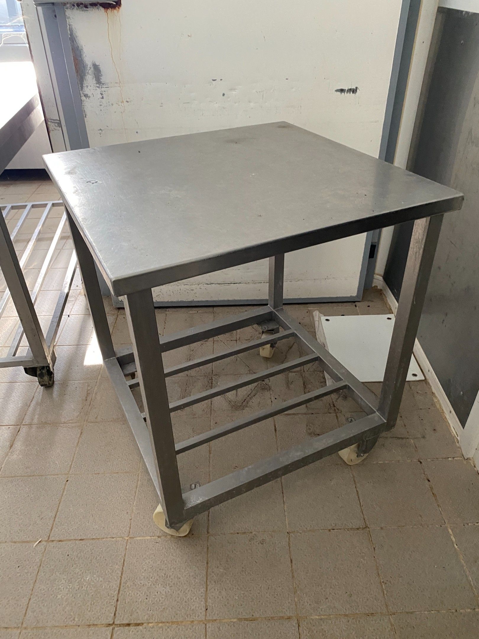 Une table carrée en inox à claies d'entrejambe, sur roulette…