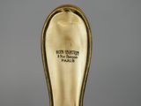 an antique gold plated spoon with a black handle on a gray surface