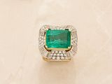 an emerald and diamond ring on a white marble surface