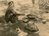 a black and white photo of a woman sitting on the ground preparing food