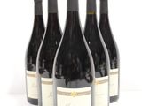 six bottles of red wine are lined up on a white surface