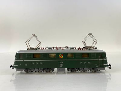 a green train that is on the tracks on a white surface