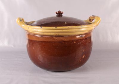un pot marron et jaune avec un couvercle, posé sur une surface blanche