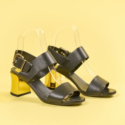 une paire de sandales noires à talon doré sur fond jaune