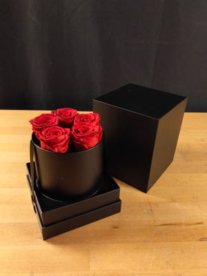 une boîte noire contenant des roses rouges, posée sur une table en bois