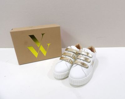 une paire de chaussures blanches avec des lanières dorées, posée à côté d'une boîte en carton