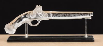 un pistolet en verre transparent posé sur un socle noir, sur une table en bois
