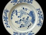 blue and white plate with flowers and birds on it on a black background
