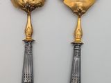 two silver and gold serving utensils on a white surface