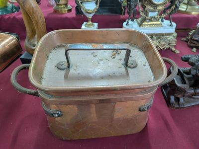 un grand faitout en cuivre posé sur une table, aux côtés d'autres objets anciens