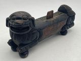 une figurine ancienne sculptée représentant un chien, montée sur roulettes, posée sur une surface blanche