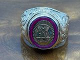 silver and pink ring with a medallion on top of a wooden table